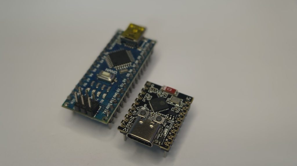 Photograph of a blue Arduino Nano board and a black USB-C microcontroller board side-by-side on a white background.
