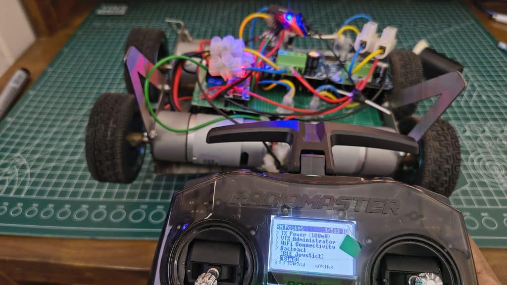 A close-up of a RadioMaster Pocket transmitter screen showing the ExpressLRS (ELRS) Lua script menu with the "Bind" option selected, positioned in front of a 4-wheel robot with active LED indicators.