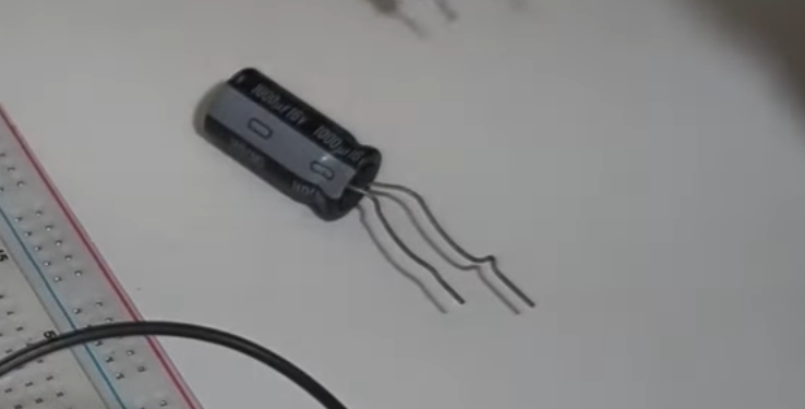 A close-up shot of an electrolytic capacitor with bent leads next to a white breadboard, ready for an electronics breadboard tutorial.