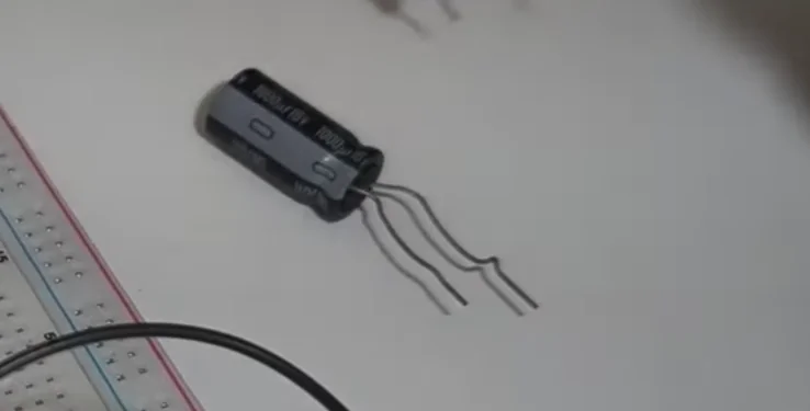 A close-up shot of an electrolytic capacitor with bent leads next to a white breadboard, ready for an electronics breadboard tutorial.